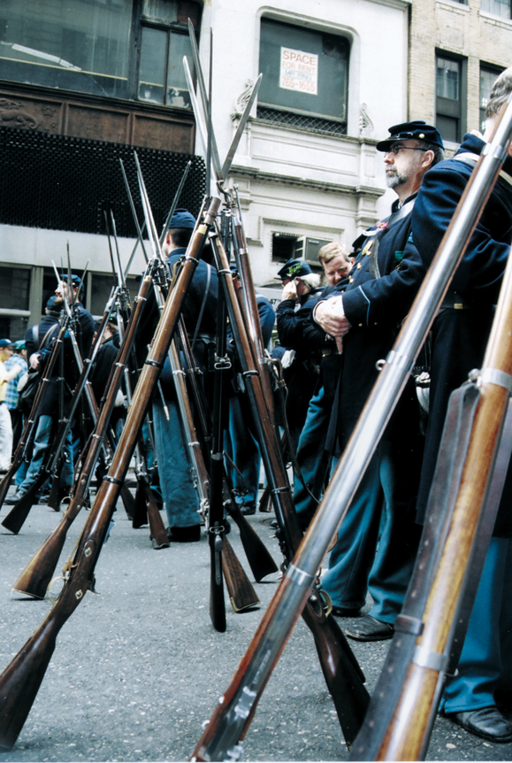 <em>Re-enactors give their muskets a rest while waiting to join the parade.</em>