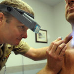 Naval Lt. Cmdr. Stephen Mannino examines a Sailor using a dermatascope and magnifying loops. Photo: Wikimedia Commons