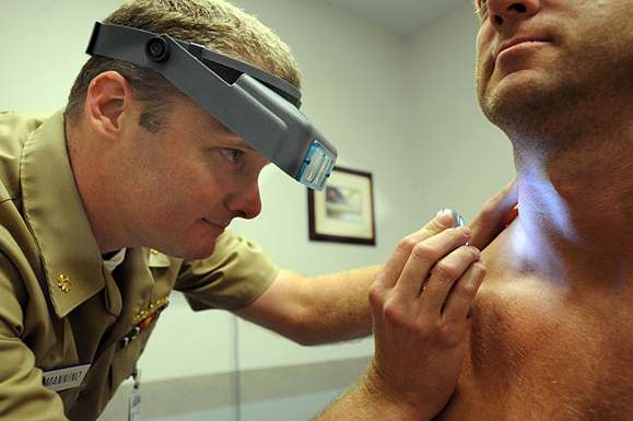 Naval Lt. Cmdr. Stephen Mannino examines a Sailor using a dermatascope and magnifying loops. Photo: Wikimedia Commons