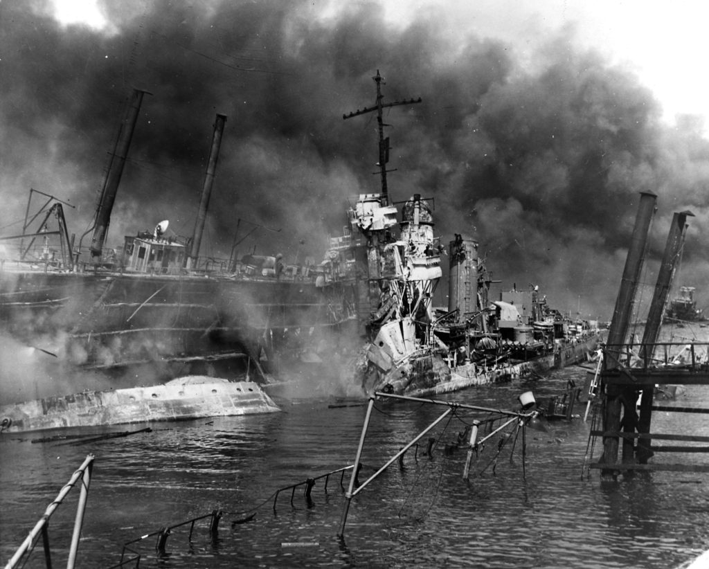 The U.S. Navy destroyer USS Shaw (DD-373) wrecked in floating drydock YFD-2 on December 7, 1941, with fires were nearly out but structure still smoking. Her bow had been blown off by the explosion of her forward magazines, after she was set afire by Japanese dive bombing attacks. In the right distance are the damaged and listing USS California (BB-44) and a dredge. Official U.S. Navy Photograph, National Archives Collection.