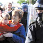 A Catholic school student and her mother make their way to Holy Cross Roman Catholic school under a heavy police and British Army presence in the Ardoyne area of north Belfast, Northern Ireland, Tuesday, Sept. 4, 2001. Protestants in the bitterly divided north Belfast neighborhood of Ardoyne hurled rocks, bricks, bottles and even flower pots at the heavily girded officers protecting the girls as they arrived for school. (AP Photo/Peter Morrison)