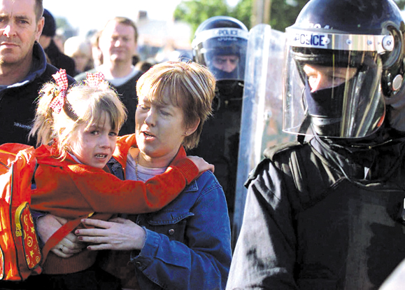 A Catholic school student and her mother make their way to Holy Cross Roman Catholic school under a heavy police and British Army presence in the Ardoyne area of north Belfast, Northern Ireland, Tuesday, Sept. 4, 2001. Protestants in the bitterly divided north Belfast neighborhood of Ardoyne hurled rocks, bricks, bottles and even flower pots at the heavily girded officers protecting the girls as they arrived for school. (AP Photo/Peter Morrison)