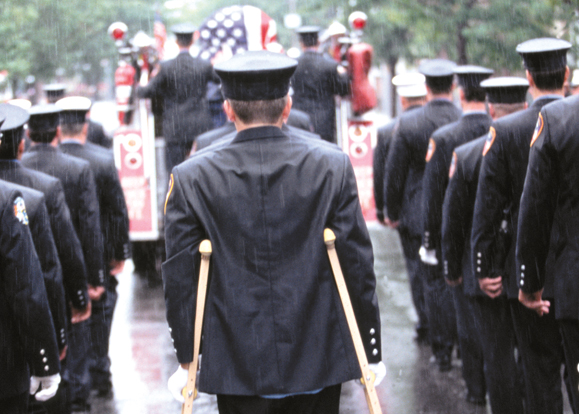 An injured fireman joins a comrade's funeral in Queens, New York; Photo - Peter Foley.