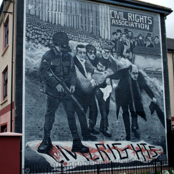 Bogside mural on Lecky Street, Londonderry. The mural depicts the famous photo of Father Edward Daly, waving a blood-stained white handkerchief as he escorts a mortally-wounded protester to safety during the events of Bloody Sunday (1972) in Derry, Northern Ireland. Photo: Wikipedia