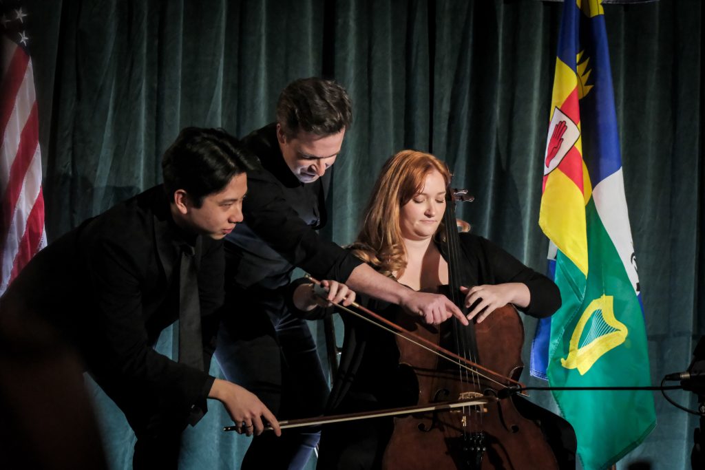 Violinist Gregory Harrington (center) with cellists Ian Lum, and Sara Scanlon (seated) performing Ravel’s “Boléro” on one cello.